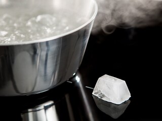 Un glaçon reposant sur la surface froide d'un plan de cuisson à induction AEG à côté d'une casserole d'eau bouillante