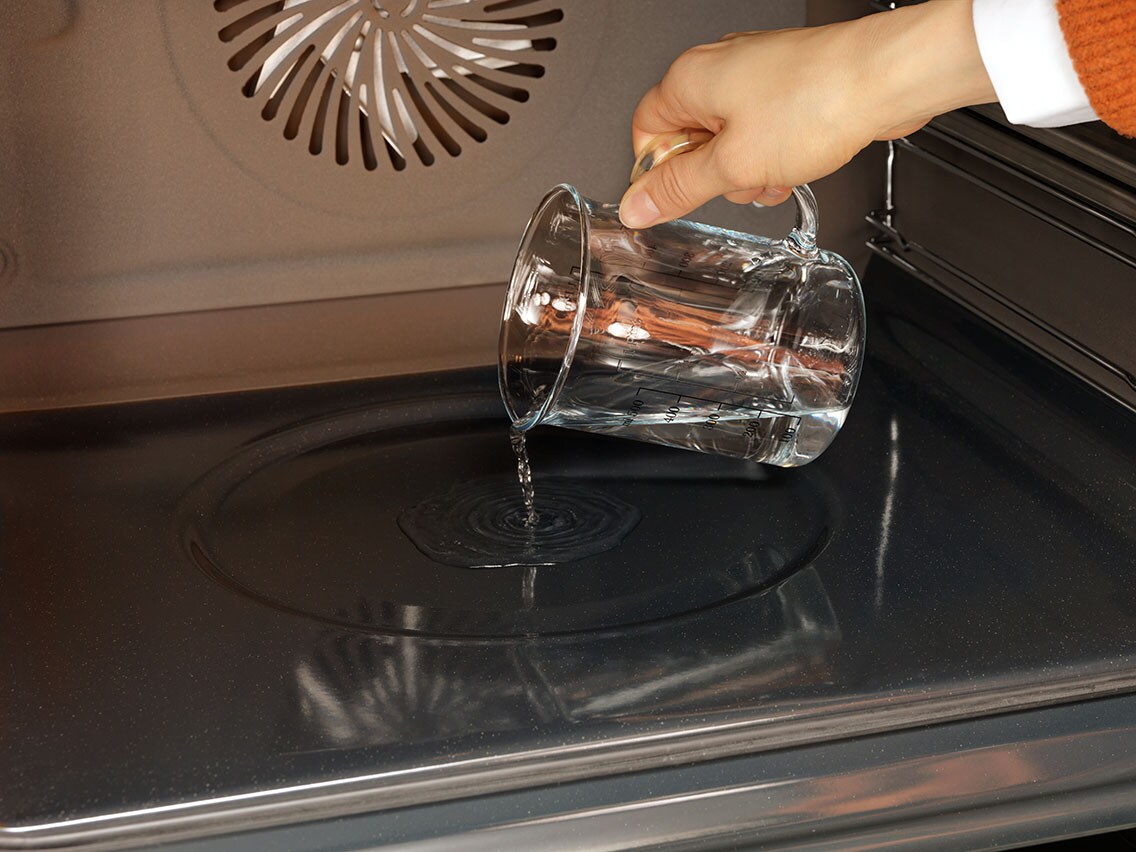 Person giesst Wasser in die Backofenmulde ein