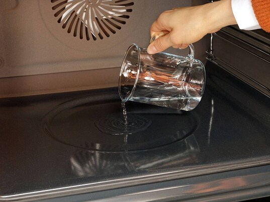 Une personne verse de l'eau dans la cavité du four