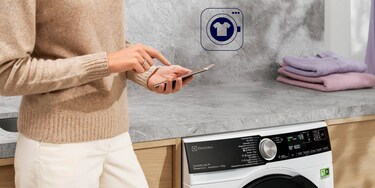 Person, die vor der Waschmaschine am Handy ist
