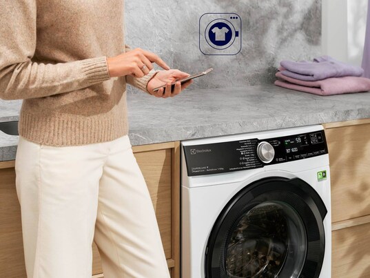 Person mit dem Handy vor einer Waschmaschine