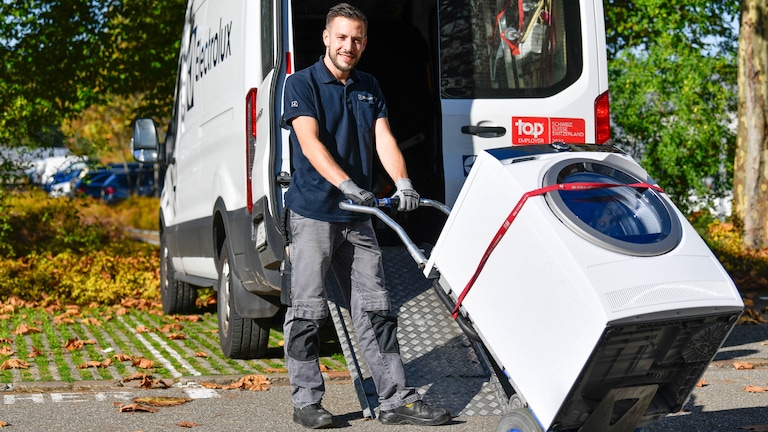 Electrolux Mitarbeiter transportiert eine Waschmaschine vor dem Electrolux Lieferwagen